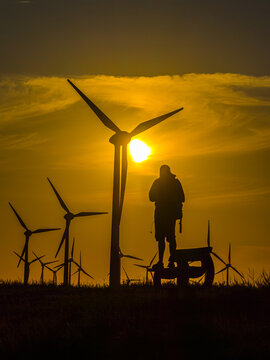 Aerial view of a person silhouetted against a golden sunset with wind turbines in a field in Emden, Niedersachsen, Germany.