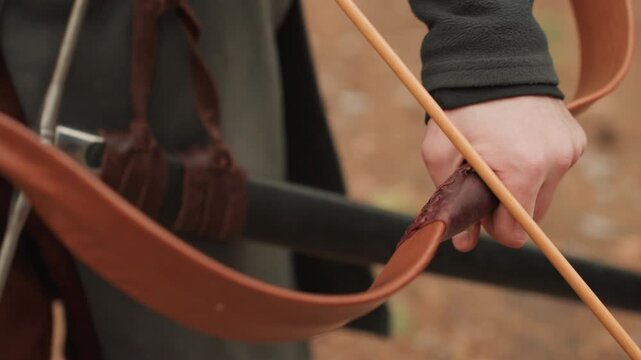 Tight horizontal view shows archer drawing wooden bow with arrow nocked, fingers gripping string and shaft, wrist rotated, forearm tense, leather gear visible, ready for controlled release outdoors