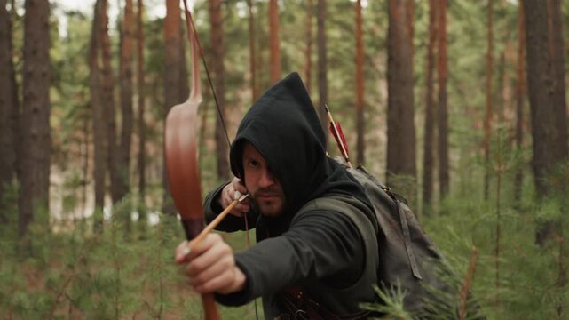 Hooded archer in rugged cloak pulls longbow to full draw while aiming rightward in pine forest, with tense forearm and back muscles, concentrated expression, soft diffused light, and natural