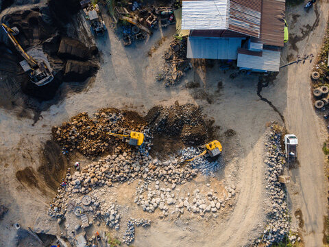 Aerial view of construction site with yellow excavators moving rocks and gravel near a building in Central Java, Indonesia.