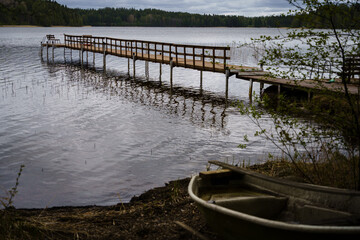 Wooden dock leading to calm lake with rowboat on foreground in Iitti, Finland © OKemppainen