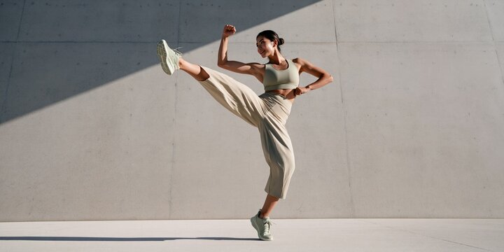 Athletic woman executing a high kick against a concrete wall outdoor fitness background for workout poster banner and active lifestyle design