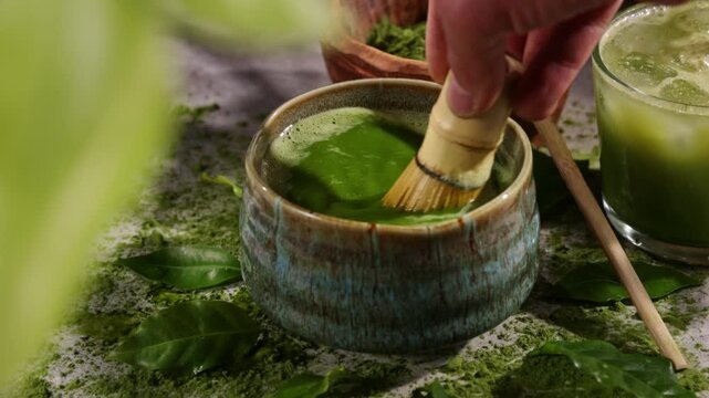 Hand whisking vibrant green matcha tea with traditional bamboo whisk, surrounded by matcha powder and tea-making ingredients. Illuminated by natural sunlight, creating an authentic tea ceremony scene