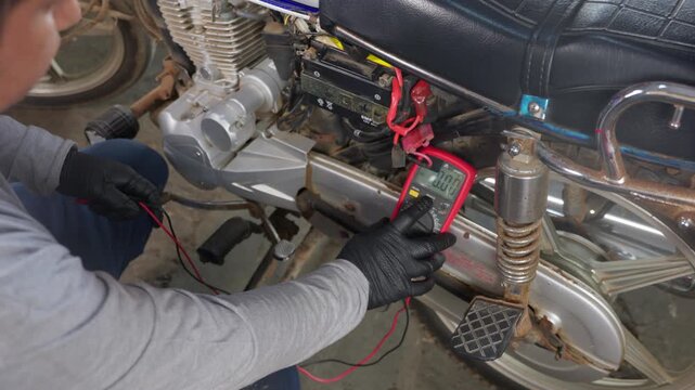 Mechanic checking motorcycle battery voltage with multimeter