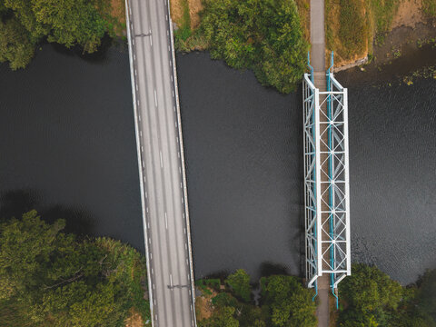 Aerial view of the Viskan river with a modern road bridge and a historic steel truss bridge surrounded by lush green trees in Askloster, Halland County, Sweden.
