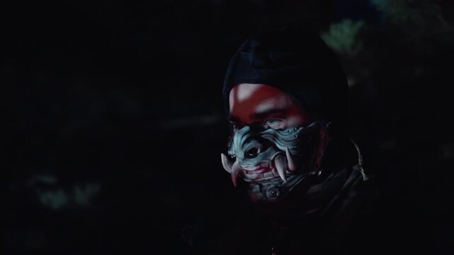 Close-up nighttime portrait of person wearing decorative patterned face mask, head slightly turned and tilted, eyes open and focused, subtle forward lean suggesting careful movement in dark moody