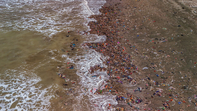 Aerial view of plastic waste and debris scattered along the shoreline with waves washing onto the beach in Indonesia.
