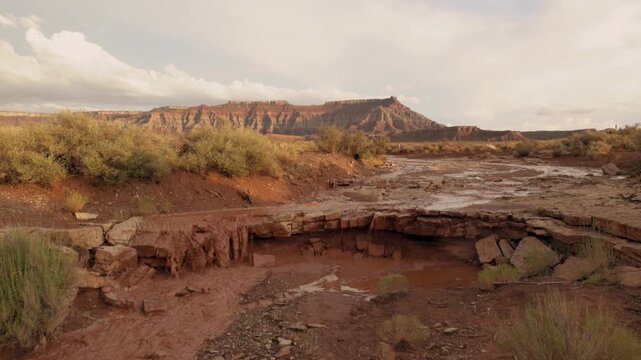 Silt laden water pours over a sandstone shelf in the desert below Gooseberry Mesa in Southern Utah USA after heavy rains during a summer monsoon storm while the clouds above begin to break up.
