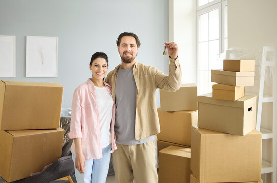 Happy couple with keys amid moving boxes. Smiling man and woman in a bright new home celebrate relocation. Boxes symbolize teamwork, start and housing success. Clear concept of new beginnings.