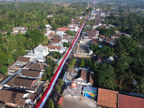 Aerial view of a long red and white Indonesian flag stretched along a street through a residential town in Wonosari, East Java, Indonesia.