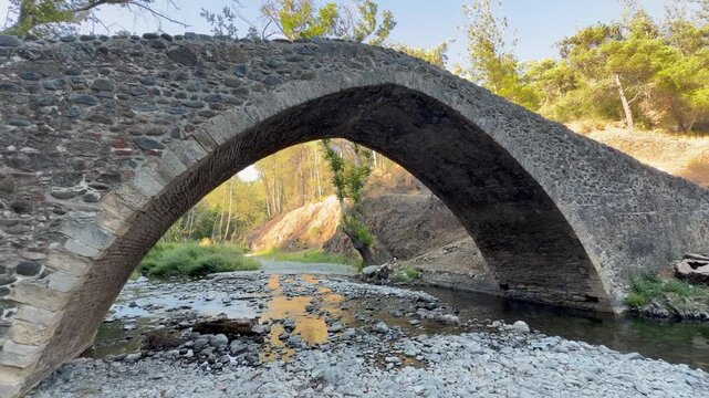 Troodos, Cyprus - August 2, 2026. Tzelefos Bridge, historic Venetian stone bridge in Troodos Mountains, Cyprus, crosses a shallow river surrounded by rocks and forest.