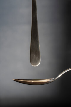 Minimalist composition with two metal spoons on dark background. Abstract macro shot of vertical stainless steel spoon handle pointing down at horizontal silver spoon against grey background