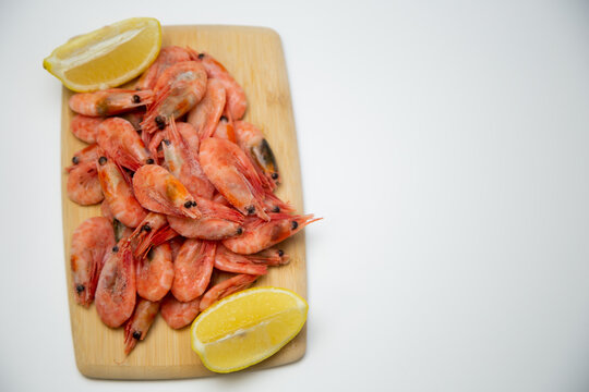 Top view of a light wooden cutting board with frozen shrimp in the center and two lemon slices diagonally. Concept: concise seafood serving. High quality photo