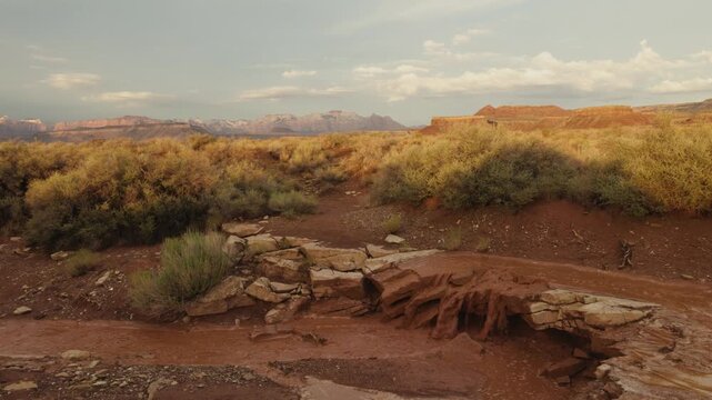 Evening shadows stretch across the desert of Southern Utah USA as the muddy water from a summer monsoon storm pours over a sandstone ledge in a shallow ravine.