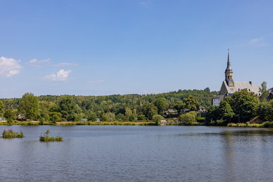 Peaceful lake waters with a church tower standing amidst lush green trees at Lac des Doyards in Belgium