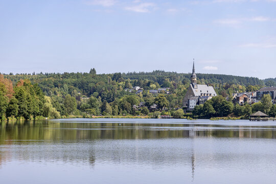 Historic church reflecting in tranquil lake waters surrounded by lush green hills at Lac des Doyards - Belgium