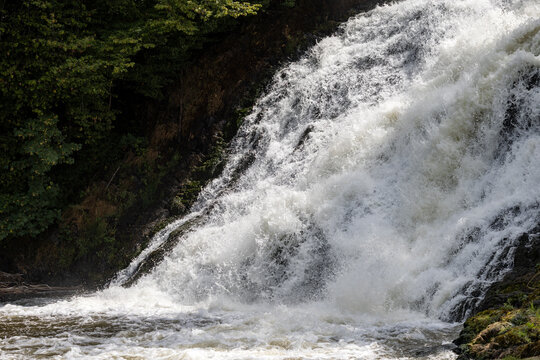 Powerful rushing water cascading down rocky slopes surrounded by forest at Les Cascades de Coo - Belgium