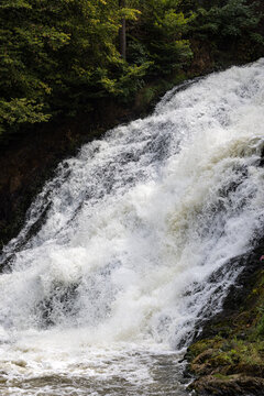 Powerful rushing water cascading down rocky slopes surrounded by forest at Les Cascades de Coo - Belgium