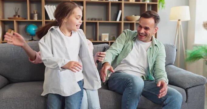 Family parents and children playing together at home. Smiling mother and father on a sofa, laughing and hugging with happiness as kids have fun. Strong family bonding and unity concept.