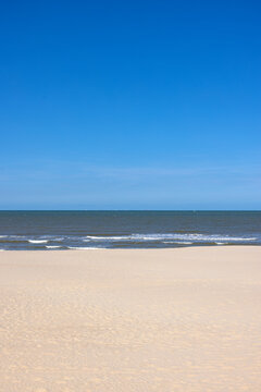 Pristine wide sandy beach under a clear blue sky stretching toward gentle ocean waves in Middelkerke - Belgium