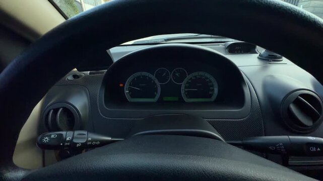 Driver seat cockpit view showing steering wheel rim, inactive instrument cluster, hood vents, stalk controls, dashboard trim, gauges, dials, glass reflections, dark interior