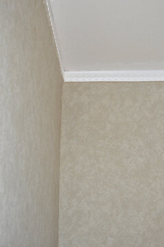 White ceiling crown molding in room corner with beige textured wallpapered walls. Interior apartment finish, home renovation, decorative stucco border, architecture and ceiling repair concept