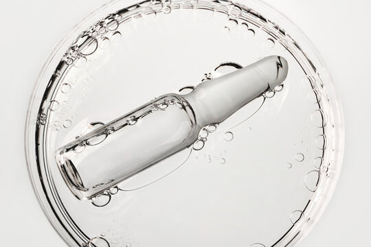 Glass medical ampoule in transparent liquid with air bubbles in petri dish