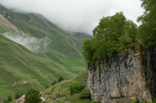 Rolling green slopes rise beneath heavy clouds and soft mist