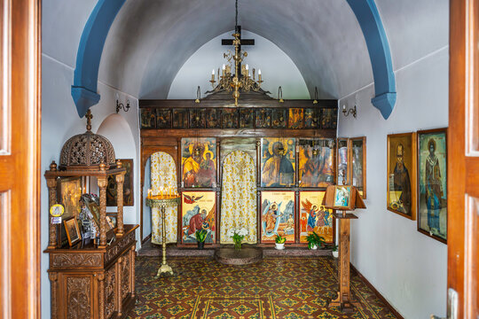 A small Greek Orthodox chapel featuring a wooden iconostasis, patterned tile flooring, and a vaulted ceiling with blue structural arches in the village of Agios Nikolaos, Greece, island of Crete.