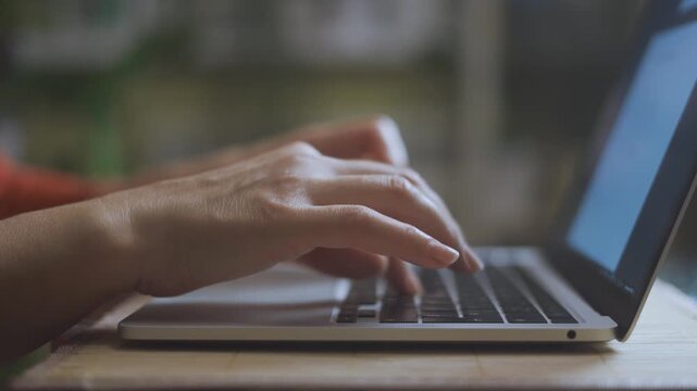 A woman types intently on a laptop. The woman s hands move quickly over the laptop keyboard in a focused environment.