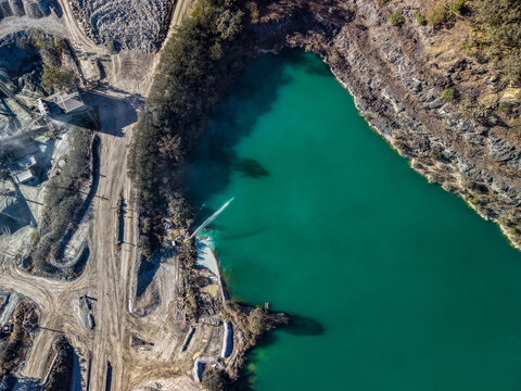 Aerial view of Holcim Australia Petrie Quarry featuring a vibrant turquoise water-filled pit, industrial dirt roads, and surrounding vegetation in Kurwongbah, Queensland, Australia.