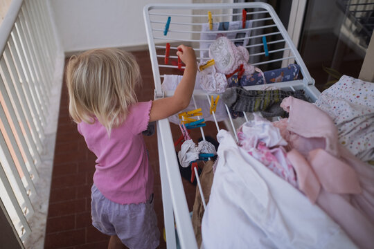 Little Girl Helping Hang Laundry on a Drying Rack on the Balcony
