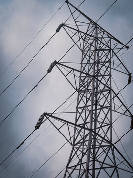 Low angle view of a tall metal electrical transmission tower with high voltage power lines against a cloudy sky