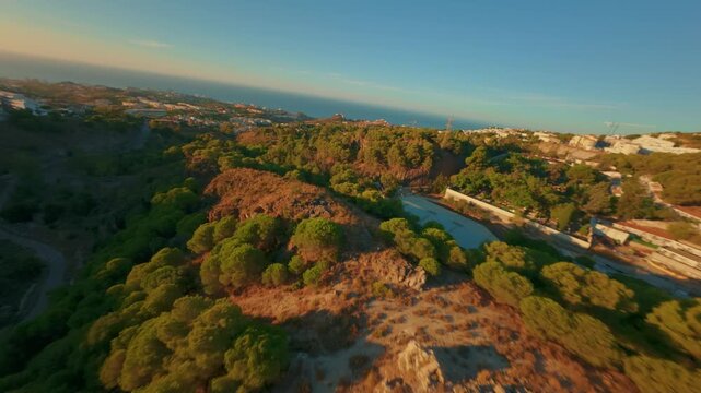 FPV-Drohnenflug &uuml;ber Autobahn und bewaldeten H&uuml;gel im goldenen Sonnenaufgang mit Aufstieg auf K&uuml;stenstadt und Meer nahe M&aacute;laga