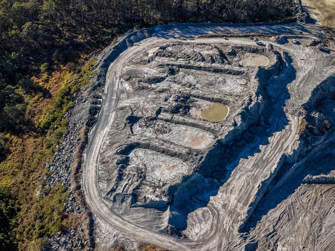 Aerial view of Holcim Australia - Petrie Quarry showing deep excavation pits, dirt access roads, and surrounding dense forest vegetation in Kurwongbah, Queensland, Australia.