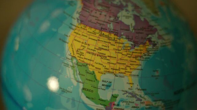 Globe spins gently, showing continents with clear labels. Yellow United States dominates the view, surrounded by oceans. Soft focus highlights the globe's smooth, colorful surface.