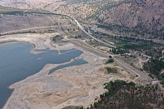 Aerial view of Clear Creek Reservoir showing low water levels with exposed shoreline, surrounding pine forests, and a nearby highway in Chaffee County, Colorado, United States.