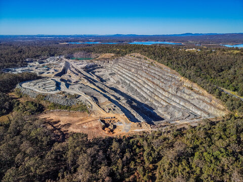 Aerial view of Holcim Australia - Petrie Quarry showing the large open-pit mine, terraced rock walls, surrounding dense eucalyptus forest in Kurwongbah, Queensland, Australia.