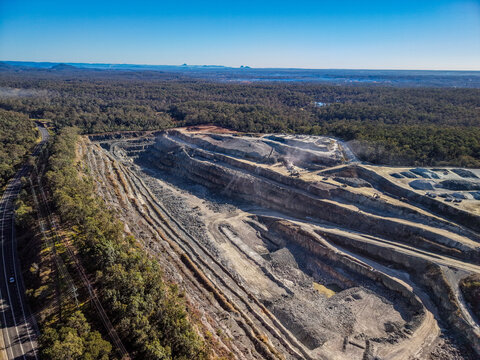 Aerial view of Holcim Australia - Petrie Quarry showing terraced rock walls, heavy machinery, and surrounding forest in Kurwongbah, Queensland, Australia.