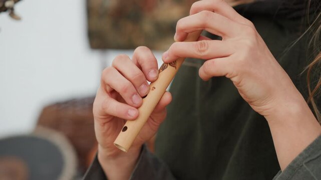 Close-up view of hands playing small wooden flute, fingers covering and lifting from tone holes to shape melody while slight fingertip blur shows ongoing movement and breath-led performance