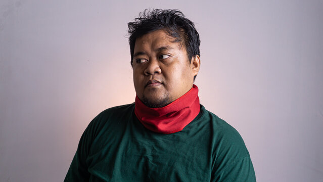 A young Southeast Asian male looks away with a subtle expression of annoyance or suspicion against a plain light grey background. The adult individual wears a dark green long sleeved