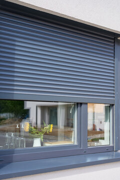 Exterior roller shutter is partly closed above kitchen window, with sunflowers and glass bottles visible inside
