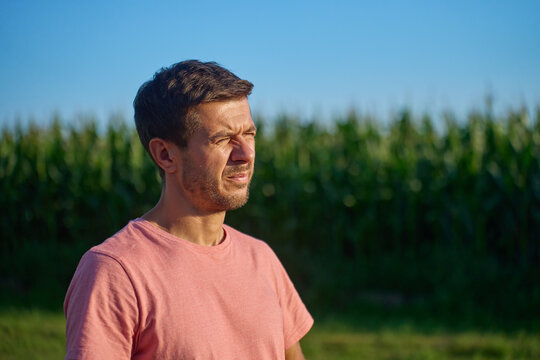 Man in pink shirt squints in bright sunlight while standing beside cornfield