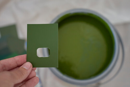 Hand holds green color sample above an open can of matching paint