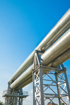 The photograph shows a pipeline on metal supports against a blue sky