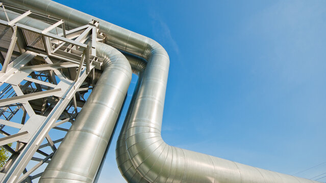 The photo shows a close-up of a straight pipeline on a metal support against a blue sky
