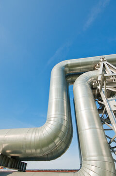 The photo shows a close-up of a straight pipeline on a metal support against a blue sky