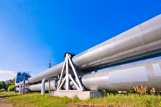 A close-up of a pipeline, with a blue sky and a power transmission tower in the background