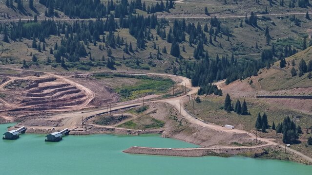 Aerial view of Mayflower Tailings Pond with turquoise water, surrounding pine forests, dirt access roads, and industrial structures in Summit County, Colorado, United States.