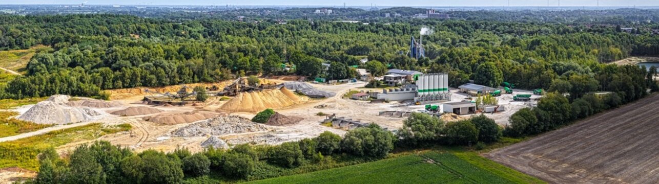 Aerial view of the ZE PAK S.A. Patnow Power Plant industrial site with concrete silos, gravel piles, and heavy machinery near forest and fields in Konin, Wielkopolskie, Poland.